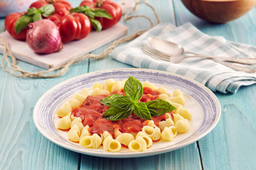 pasta conchiglie type with tomato sauce on an aqamarine wooden table surrounded by fresh tomatoes and onion