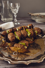 mince meatball on a spit (Italian dish) surrounded by glass, dishes and cuttlery, an elegant napkin on the table. everything on a gray wooden table with a gray background..