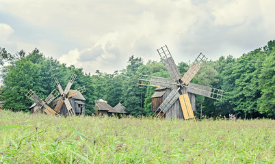 Windmills close up, green forest, wild vegetation, blue clouds sky