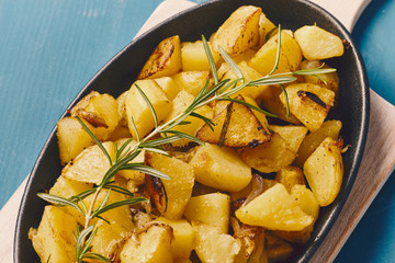 roasted potatoes iwith onion and rosemary in a cast iron pan over a white chopping board on a blue table