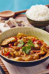 Curry chopped pork in a bowl with basmati rice on a bamboo placemat on a blue wooden table