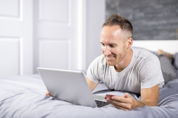 Serious casual young man using laptop in bed at home