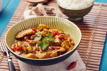 Curry chopped pork in a bowl with basmati rice on a bamboo placemat on a blue wooden table