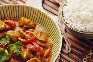 Curry chopped pork in a bowl with basmati rice on a bamboo placemat on a blue wooden table