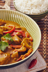 Curry chopped pork in a bowl with basmati rice on a bamboo placemat on a blue wooden table