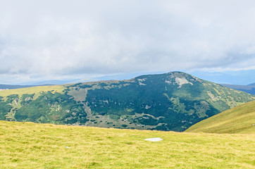 Obraz premium Parang Mountains in the clouds, hills with green grass and rocks