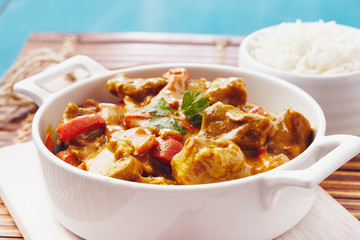 Curry chopped pork in a bowl with basmati rice on a bamboo placemat on a blue wooden table
