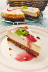 new york cheesecake with cherry sauce on a plate on a blue wooden table, full cake in background