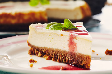 new york cheesecake with cherry sauce on a plate on a blue wooden table, full cake in background