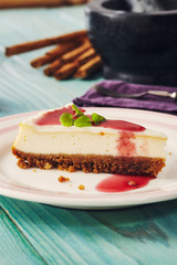 new york cheesecake with cherry sauce on a plate on a blue wooden table, full cake in background