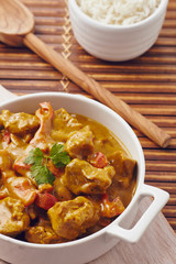 Curry chopped pork in a bowl with basmati rice on a bamboo placemat on a blue wooden table