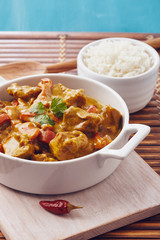 Curry chopped pork in a bowl with basmati rice on a bamboo placemat on a blue wooden table
