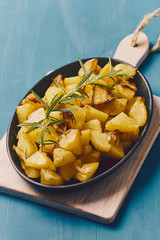 roasted potatoes iwith onion and rosemary in a cast iron pan over a white chopping board on a blue table