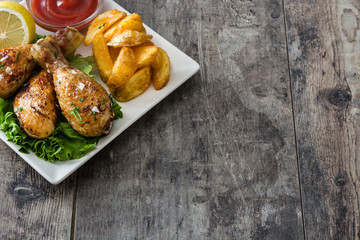 Roast chicken drumsticks and chips on wooden table

