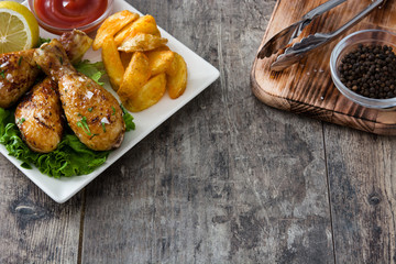 Roast chicken drumsticks and chips on wooden table

