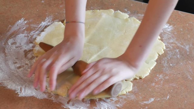 Baker kneading dough with rolling pin on table prepares bread or apple pie
