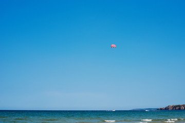 Parachuting over a sea, towing by a boat. Paragliding in the clear sky above the sea. Riding on a parachute behind a boat.