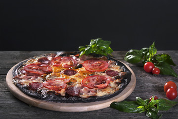 Black pizza with salami, ham, tomato and cheese