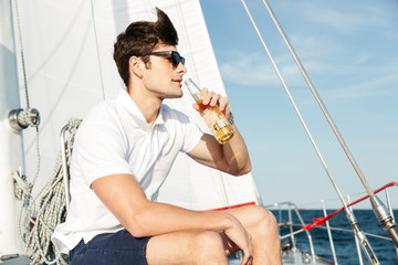 Handsome young man drinking beer while resting on the yacht