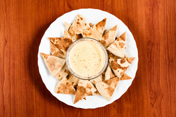Delicious homemade nachos with spicy cheese sauce on a round white plate. Traditional Mexican food, top view