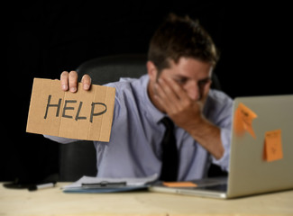 tired desperate businessman in stress working at office computer desk holding sign asking for help