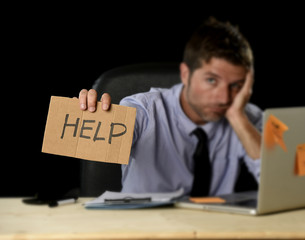 tired desperate businessman in stress working at office computer desk holding sign asking for help