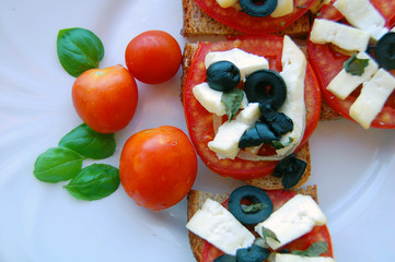 Bruschetta with tomatoes, black olives, goat cheese, herbs and oil on toasted bread