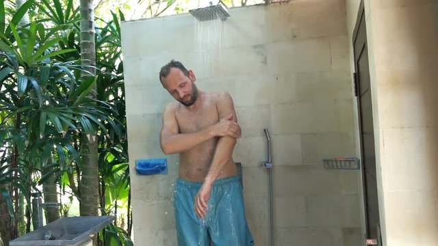 Young man washing his arms standing under shower in the garden, super slow motion

