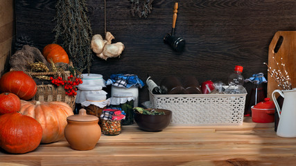 Domestic stocks with marinated vegetables in glass jars on a wooden shelf. Pantry. Pumpkins, dishes, boxes, old things. Many items