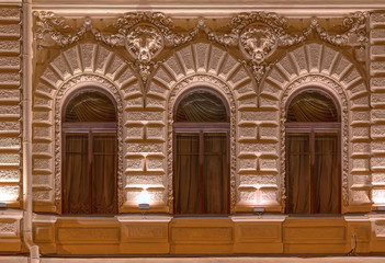 Three windows in a row on night illuminated facade of urban office building front view, St. Petersburg, Russia.