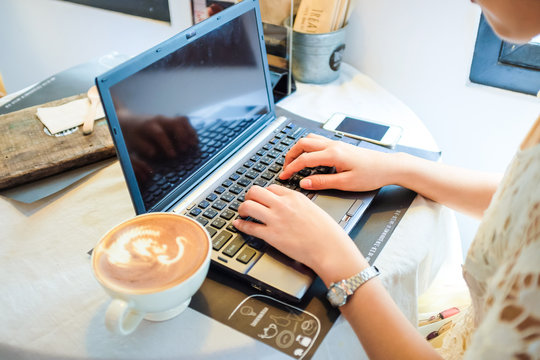 Women hand with latte coffee cup on the table about laptop