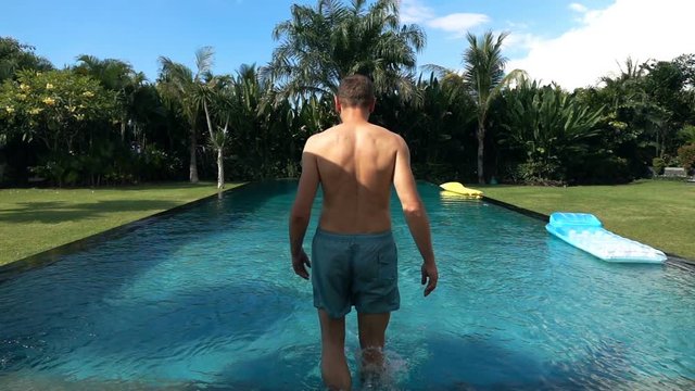 Young man walking into swimming pool, super slow motion 
