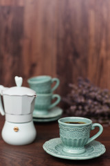 Cup of coffee and Italian coffee maker in blue, scent of lavender. Dark wooden background