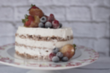 Blurred naked cake with caramelized fruits - strawberries, blueberries, raspberries. Sponge cream cake in floral high plateau, tray. Rustic background
