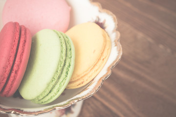 French macaroons in a vintage bowl on wooden rustic table. Retro toned image.