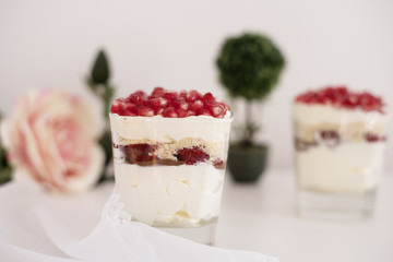 Homemade layered dessert with mascarpone, chocolate, cream, fresh strawberries, cookies, pomegranate. Cheese in a glass. White background, high key, selective focus