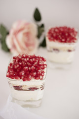 Homemade layered dessert with mascarpone, chocolate, cream, fresh strawberries, cookies, pomegranate. Cheese in a glass. White background, high key, selective focus