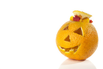 Food art creative concept. Halloween scary face carved into yellow orange fruit with food decorations isolated over a white background