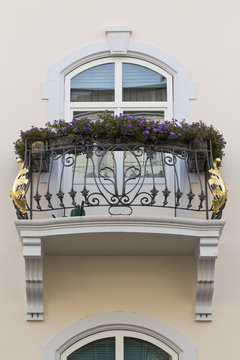 Ein einzelner Balkon an einem privaten Stadthaus mit Metallgeländer, goldenen Verzierungen und Blumen