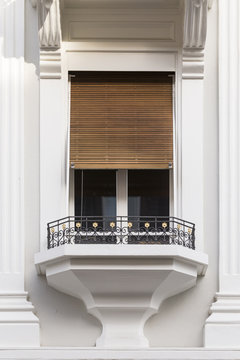 Ein einzelner kleiner Fensterbalkon mit verziertem Geländer an einem weiss gestrichenen Herrenhaus