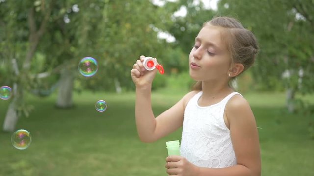 A cute girl blows a bubbles in the garden.
