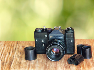 Old retro photo camera and film negative strip on wooden table against green blurry background.