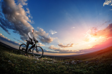 Naklejka na ściany i meble cyclist standing with mountain bike on trail at sunset