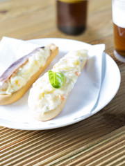 A plate with a typical spanish ensaladilla rusa, russian salad, on a wooden table accompanied by beer. A appetiser of Spain called marinera with anchovy or without it