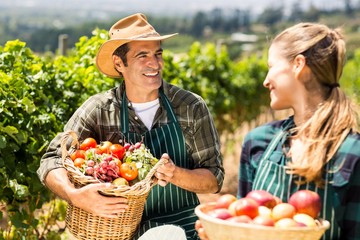 Happy farmer couple holding baskets of vegetables and fruits