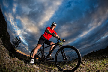 Fototapeta premium cyclist standing with mountain bike on trail at sunset