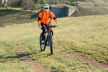 Naklejka na ściany i meble Bicycle tourist with loaded bike riding on green meadow
