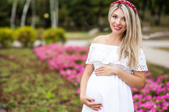 Beautiful lovely girl wearing her first child in the stomach and is looking forward to his birth. Strolling in the park, enjoy nature and quietness
