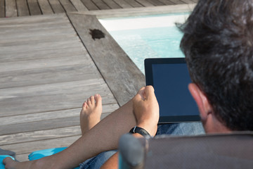 Back of a man sitting by pool with digital tablet
