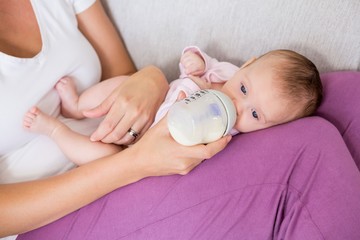 Mother feeding baby with milk bottle in living room